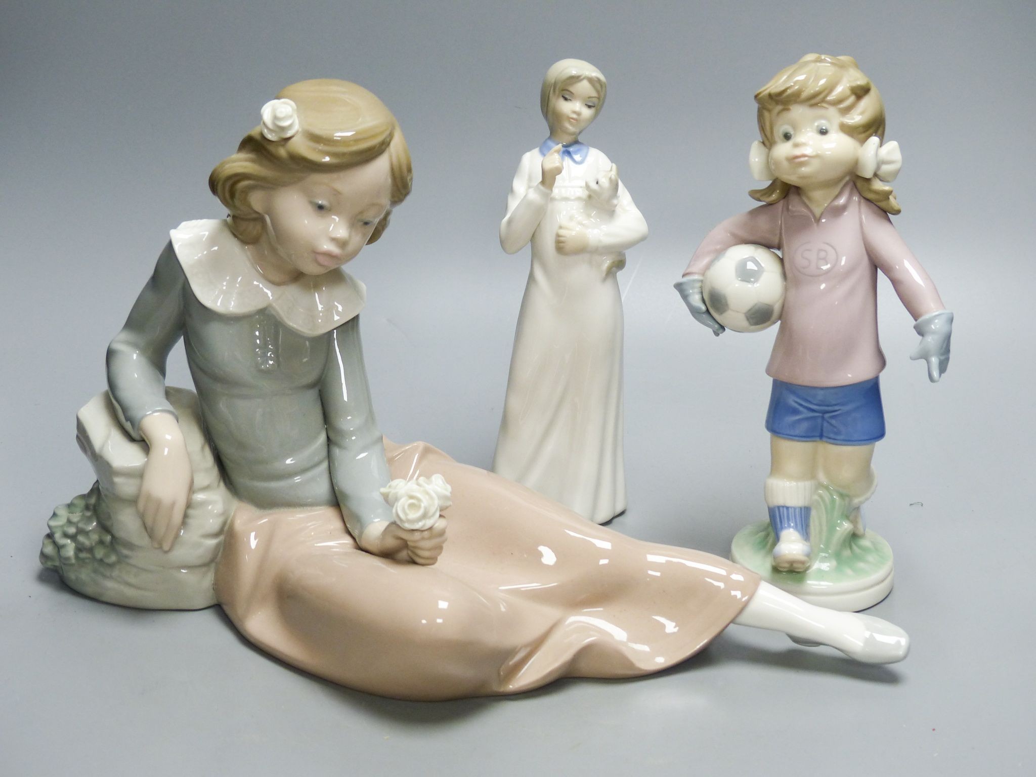 A Lladro figure of a girl holding a football, a large Nao figure and one similar Spanish figure.